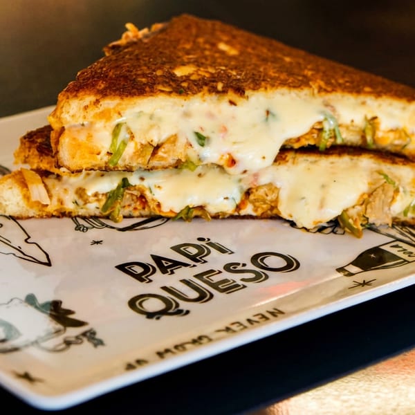 A grilled cheese sandwich, cut in half, oozing with melted cheese and green peppers on a branded plate.