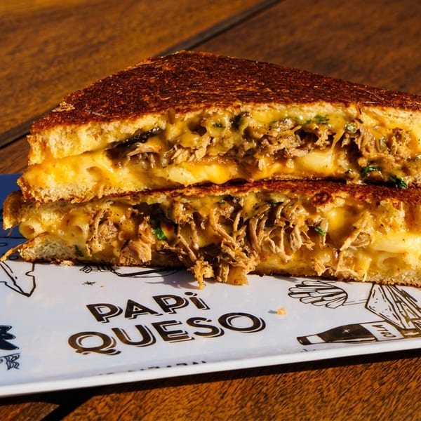 A Papi Queso grilled cheese sandwich, cut in half, revealing melted cheese and pulled pork.