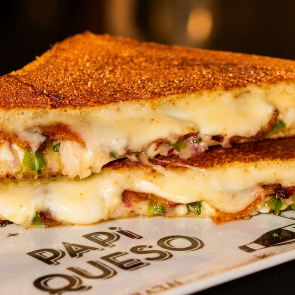 Golden-brown grilled cheese sandwich, cut in half, oozing melted cheese with green and red fillings.
