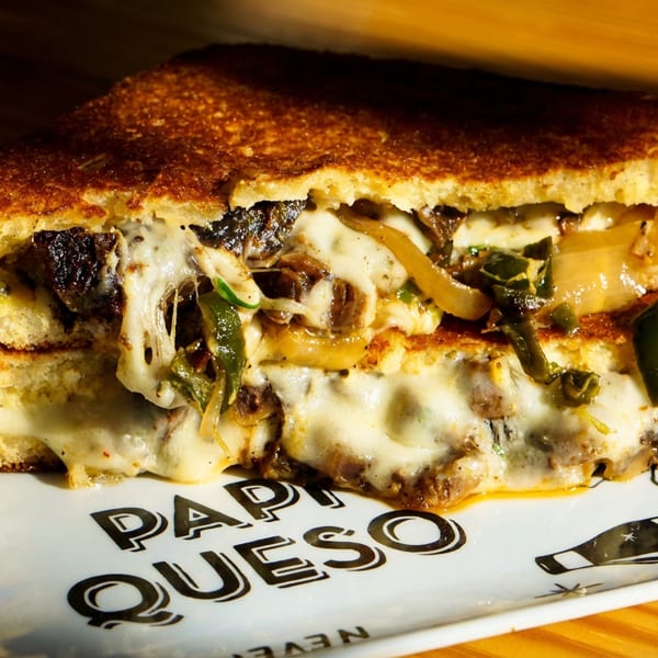 Grilled cheese sandwich with melted cheese, caramelized onions, and green peppers on a white plate.