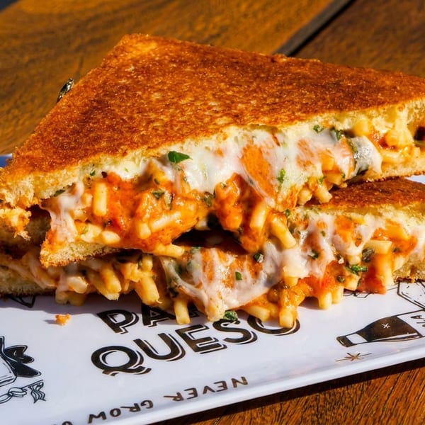 A grilled cheese sandwich filled with macaroni and red sauce, cut in half on a white plate.